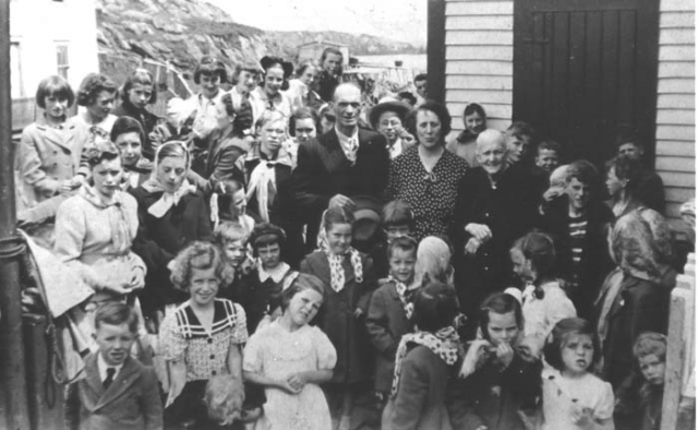 081: Children's party hosted by Tom and Anne Dunphy to celebrate their daughter Mary's  wedding in the States. (1952) [courtesy of Mary (Dunphy) Lamb]  Back row l-r Clarissa Ennis (straight hair), Anita Norman, Teresa Kerrivan (dark coat),  Gwen Carroll holding baby Ron? Ryan, Mary Ennis, Babe Ennis, Anne Counsel (black hat),  Kathleen Barry, Noreen Ryan; 2nd row from back l-r Beth Lambe, Mary Finn, Madonna  Whelan (white kerchief), Rita Whelan (ribbon on hair, looking to right), Madonna  McCarthy (blonde), Mary Reddy, Imelda Ryan (behind Tom Dunphy), Vince Carroll (wide  brimmed hat), unidentified (face over Vince's shoulder), unidentified (behind Vince),  Adrian Ryan (looking from around office corner; adults l-r Tom Dunphy, Anne (Carroll)  Dunphy, Mrs. Stasia Dunphy; behind Stasia l-r Teresa Norman, Willie Barry, Ray Carroll,  Joe Barry (hand on cap brim), Vince Ennis (stripes), Francis Bishop, Joe Rose,two  unidentified girls (kerchiefs, faces not showing); front row l-r Michael Norman,  Winnie Norman holding Brendan Norman, John (or Aloysius) Ryan (blonde behind Winnie),  Veronica Kerrivan ? (black hat), Hilda Whelan (front center), Irene, Ethel and Claire  Webber (matching polkadot kerchiefs), Rita Ennis (by Tom Dunphy's hat), unidentified  (kerchief, face not showing), Sheila Ryan (hand to mouth), Bertha Norman (behind Sheila,  looking left), Carmelita Spurvey (braids, back to camera), Phyllis Whelan (front),  Ethel Lambe (front, far right).  - person named as baby Ron? Ryan, born 1951, also named as Myra Carroll.  - person named as Imelda Ryan also named as Gertrude Ryan.  - person named as Francis Bishop, born 1943, also named as Joe Barry, born 1940,  Charles Norman, born 1939, and Jerome Mulrooney, born 1964.  - person named as Brendan Norman, born 1950, also named as Adrian Norman, born 1944.  - person named as John Ryan also named as Aloysius Ryan.  - person to right of John Ryan has been named as Gertrude Ryan, born 1950, and Eileen  Ryan, born 1950